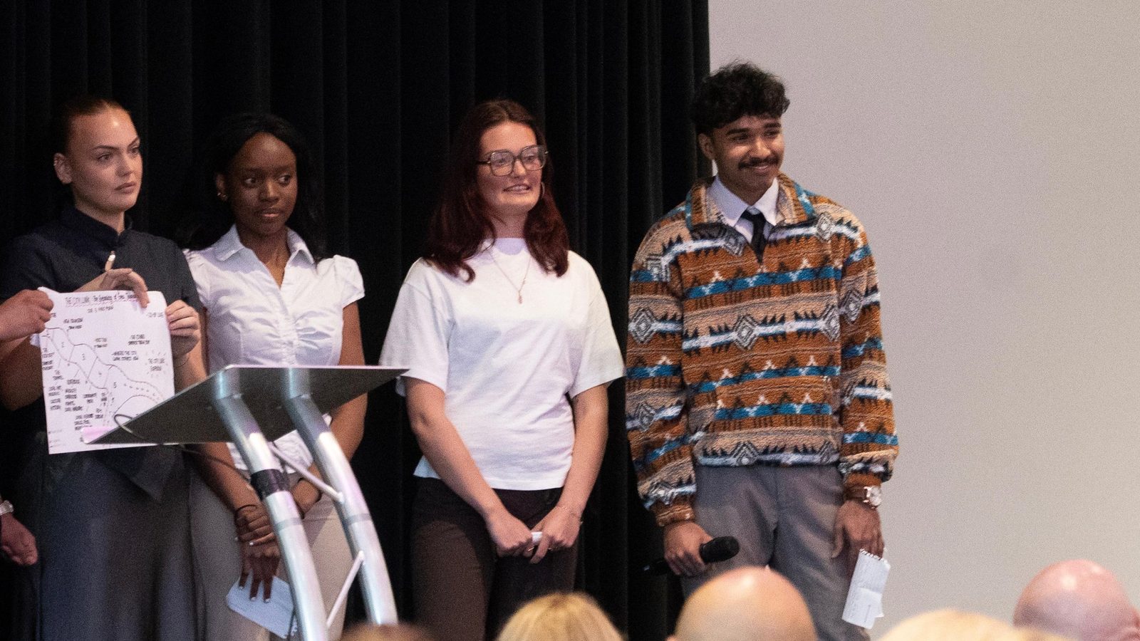 Goutham on stage with his teammates, holding a microphone, presenting to an audience.